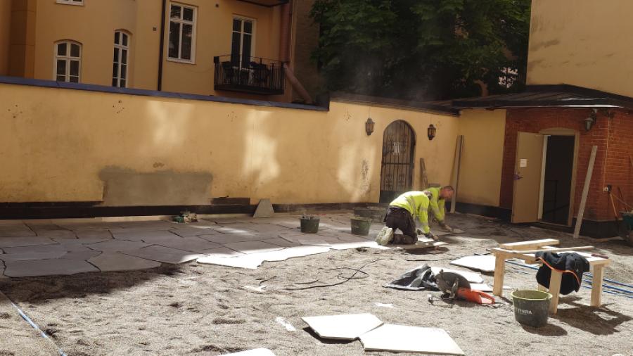 Gården den 15 maj 2025 under gårdsrenoveringen. Två plattläggare i farten,