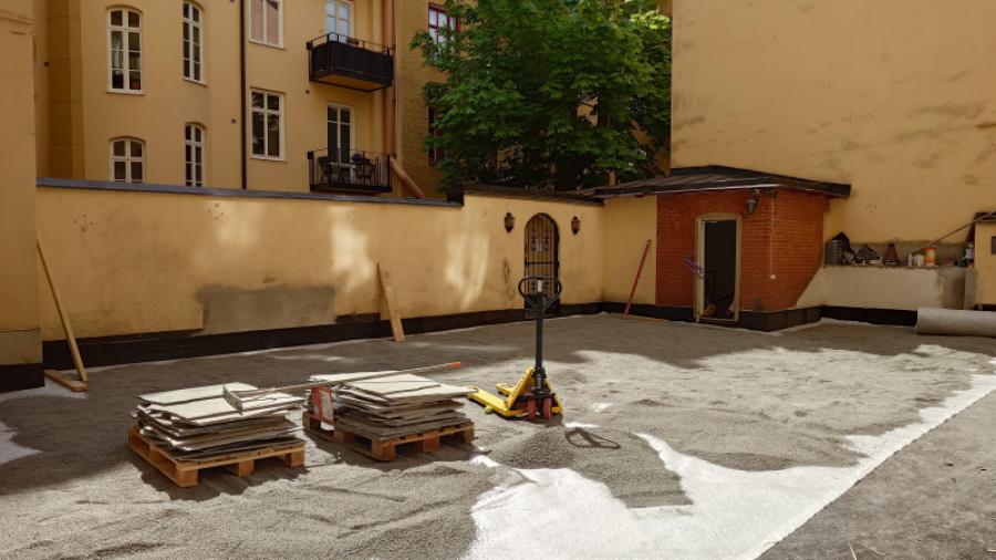 Gården den 12 maj 2025 under gårdsrenoveringen. Lastpallar med plattor.